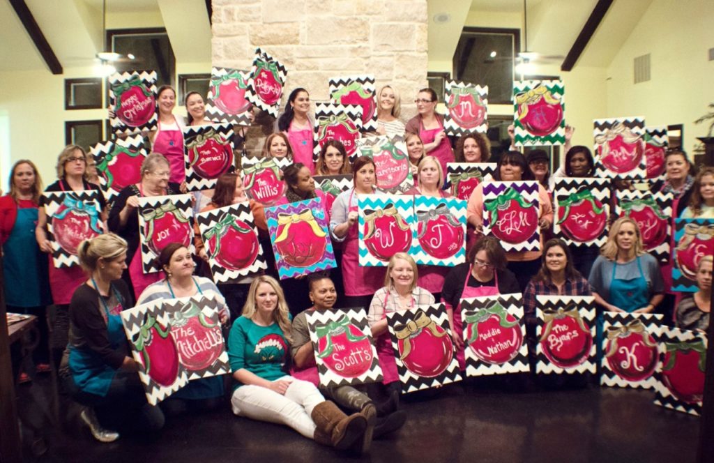 huge group of women holding finished canvases at a paint party