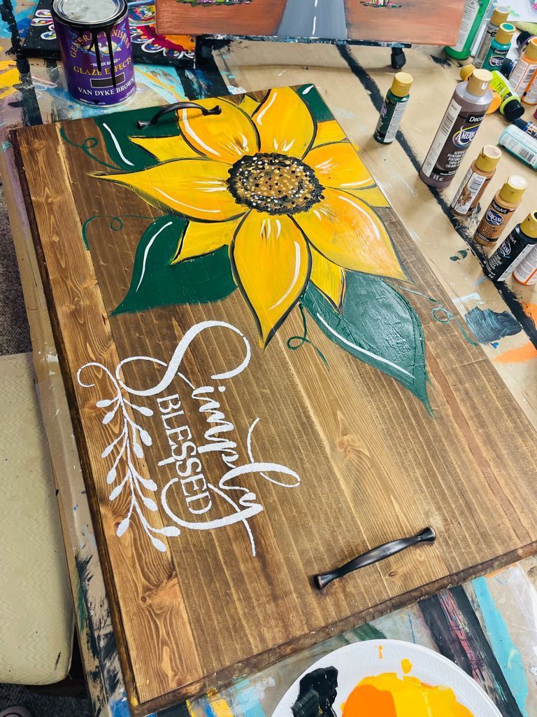 noodle board with hand painted sunflower and stenciled words "simply blessed" and bottles of acrylic paint